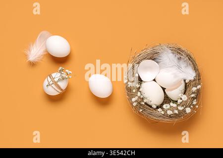 Nest with Easter eggs, shell, feathers and gypsophila flowers on orange background Stock Photo
