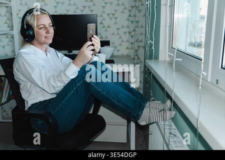 Business woman stretching her arms while sitting on her office chair at her desk in her home office, taking a break from work and relaxing her muscles and drinking coffee during her break. Stock Photo