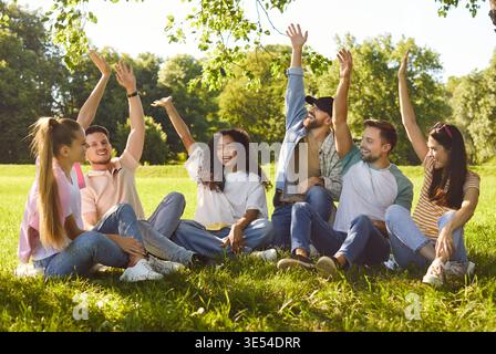 Happy diverse group of friends, people sitting together in circle, green sunny outdoor park Stock Photo