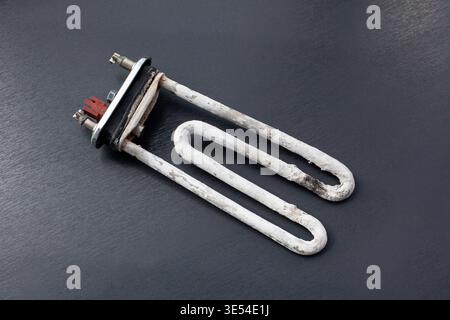A burned heating element from a washing machine is shown on a dark surface. The element is damaged and shows signs of wear and damage from use. Stock Photo