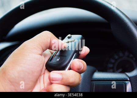 Remote Car Key Control, A hand holds a modern black remote car key, pressing the lock button inside the driver's cabin with the steering wheel in the Stock Photo