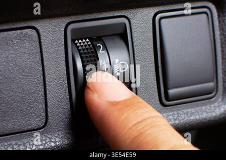 Car Headlight Leveling Switch, A close-up of a finger operating a manual headlight leveling thumbwheel switch on a car dashboard to control beam heigh Stock Photo