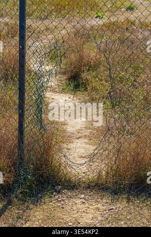 Open Gap Hole in Mesh Wire Fence With Footpath in Dirt Land Stock Photo