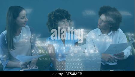 Reviewing 3 colleagues in business casual studying charts on sofa in office, with digital overlay Stock Photo