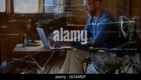 Man typing on laptop in cabin, bringing HUD overlays with code, waveforms, map dots for coding Stock Photo