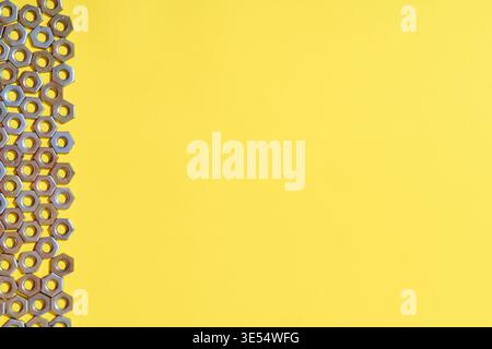 Metal nuts arranged in vertical border composition on yellow background with large copy space Stock Photo