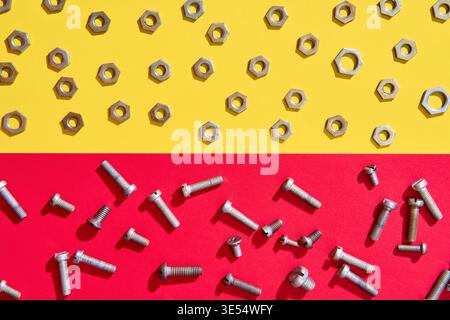 Mixed screws and nuts scattered across red and yellow background in minimal industrial style Stock Photo