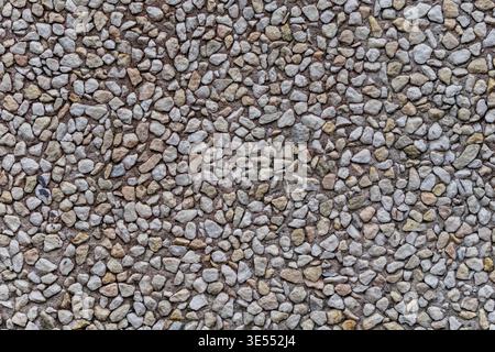 Close up of small pebbles embedded in concrete forming a rough mosaic surface. Natural stone texture with varied tones and granular detailed pattern. Stock Photo