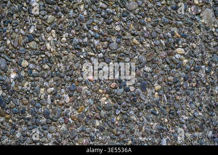 Close up of dark concrete surface with embedded multicolored pebbles. Stock Photo