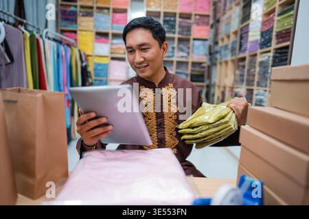 seller using tablet while sitting on a desk with his product Stock Photo