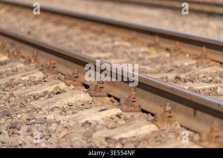 Close macro of rusty railway rail foot and coarse ballast, oxidation textures and weathered metal contrasts ideal for vintage industrial visuals. Stock Photo