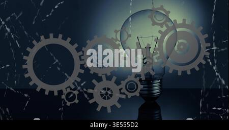 Glowing clear incandescent bulb with filament casting halo on dark tabletop, gears overlay Stock Photo