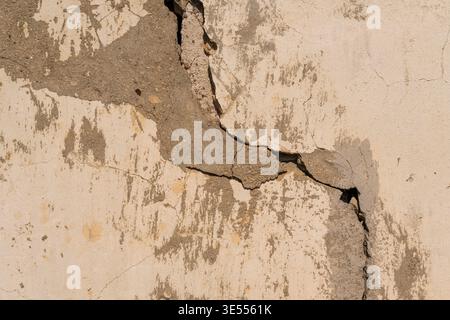 Cracked beige plaster wall with fissure, granular edges, peeling layers, warm sepia tones, highresolution detail for gritty minimalism and texture ove Stock Photo