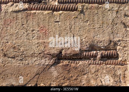 Textured concrete surface with rusty reinforcement closeup highlighting honeycomb pores, ochre patina, linear steel ribs, highcontrast relief, weather Stock Photo