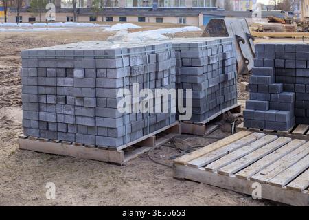Concrete paving blocks stacked on wooden pallets at a construction site. Grey sidewalk tiles secured for transportation, ready for urban landscaping a Stock Photo