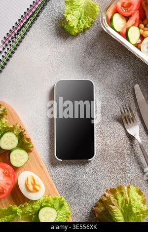 Weight loss concept, calories counting, diet, food control and Calorie counter application on smartphone with salad, egg and vegetable. Top view. Copy space. Vertical . Stock Photo