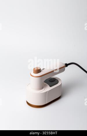 Modern compact white travel garment steamer with wooden accent and gold trim, standing on its base against a clean white background. Stock Photo