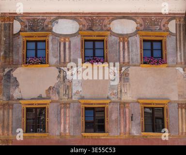 Skofja Loka, Slovenia - 30 July 2025: Decorated historic building facade with painted murals, classical columns, yellow-framed windows and pink flower Stock Photo