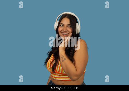 Young woman smiling while wearing headphones and enjoying music on blue background Stock Photo