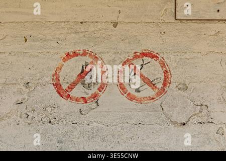 Two faded, red, spray-painted general prohibition signs on a textured concrete wall, Saaremaa, Estonia, Europe. Stock Photo
