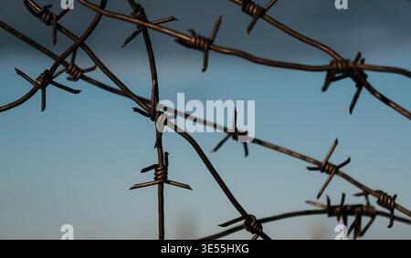 Wire fence stands against a blue sky and clouds in a rural area at dusk Stock Photo