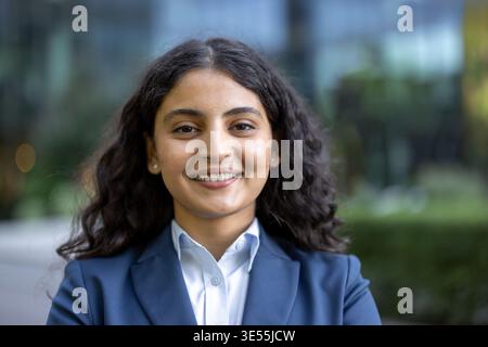 Confident businesswoman smiling while posing for a professional portrait, wearing a blue suit and white shirt, representing success and professionalism in a corporate environment Stock Photo