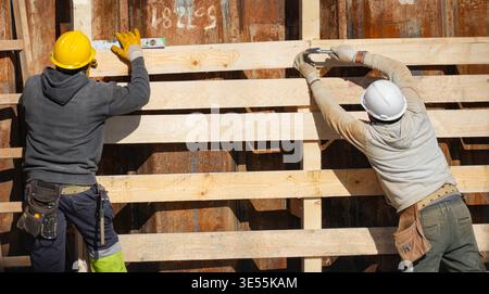 Two builders working on wooden construction, vividly showing the example of teamwork and occupational safety. Stock Photo