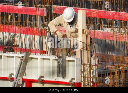 A constructor working with tools on building site with red wooden formwork, showing a heavy working process. Stock Photo