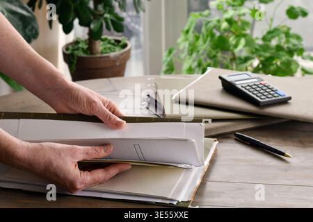 Woman hands searching through file folder on table in home setting. Documents and paperwork visible, highlighting organization, record keeping, and ev Stock Photo