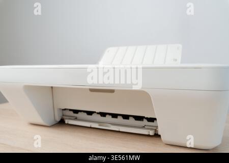 Compact white home printer on a wooden desk with an open paper tray, illustrating minimalist office equipment and modern printing technology ideal for Stock Photo