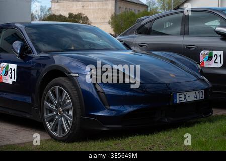 Valmiera, Latvia-April 26,2025-Dark blue Porsche Taycan electric car with Latvian license plate parked outdoors at a car event next to a gray Porsche Stock Photo