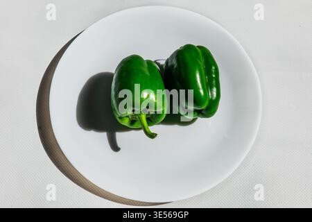 Assorted fresh organic vegetables including red tomatoes, green bell peppers, and orange carrots arranged on white plates and wooden cutting boards, m Stock Photo