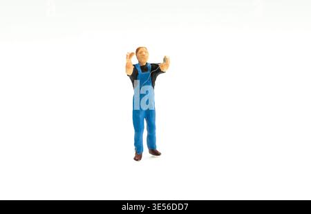 Miniature Worker Figurine in Blue Overalls Standing on White Background Raising Arms for Model Scene Stock Photo