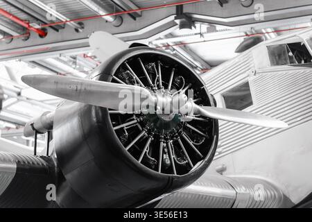 Propeller and wing of an old aircraft in a hangar. Close-up view of silver-colored 1930s vintage airliner under a metal roof of spacious hangar. Stock Photo