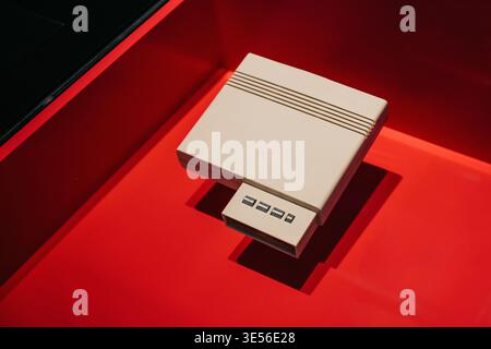 Vintage cream-colored gaming console on red background. A high-angle shot of a classic 8-bit style video game console - beige design with ridges. Stock Photo