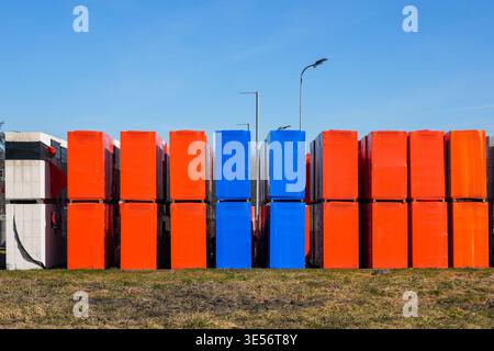 Neatly arranged stacks of orange and blue construction materials on pallets, forming a bold geometric pattern under clear sky Stock Photo
