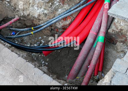 Underground utility cables and red conduit pipes in trench during urban infrastructure construction Stock Photo