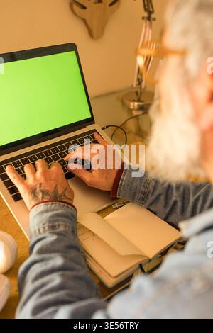 Senior man working at home desk using laptop with green screen Stock Photo