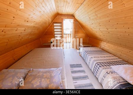 Homestay bedroom with wooden walls, two beds, soft light, and warm rustic interior Stock Photo