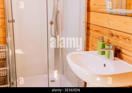 Cozy wooden cabin bathroom with modern shower cabin, sink, and natural warm interior design Stock Photo