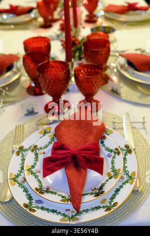 Long Christmas table view showing red glasses, tall candles and elegant place settings. Stock Photo