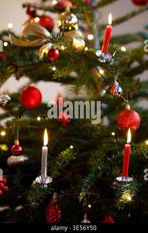 Lit red and white candles glow warmly on a decorated Christmas tree with ornaments. Stock Photo