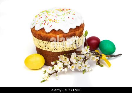 A cake with frosting and sprinkles stands beside colorful eggs and spring blossoms for an Easter celebration during the holiday. Stock Photo