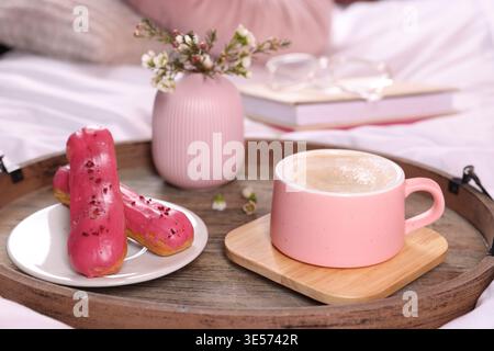 Aromatic coffee in cup, eclairs, and beautiful flowers on bed, closeup Stock Photo
