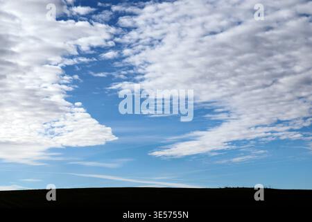 Vast sea of fluffy white clouds rolls over dark green hills under brilliant blue sky expanse above. Bor et Bar. France. Stock Photo