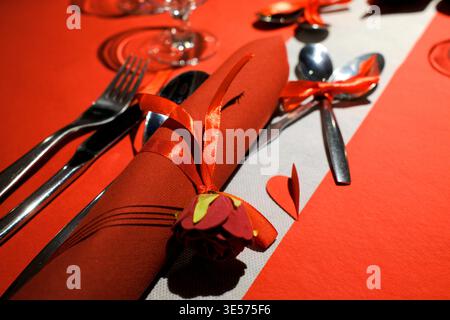Elegant red Valentine's Day table setting with satin ribbon-wrapped napkins and rose decorations. Stock Photo