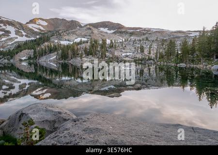 A mountain range with a lake in the foreground. The lake is calm and the reflection of the mountains can be seen in the water. The sky is cloudy and t Stock Photo