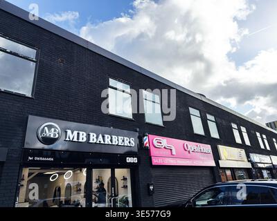 Manchester, UK - February 22, 2026: Street view of MB Barbers storefront and neighboring shops on a black brick high street in Manchester UK. Stock Photo