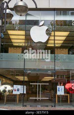 Exterior view of an Apple Store featuring the iconic Apple logo on a modern glass facade. The storefront includes glass doors and large windows with Stock Photo