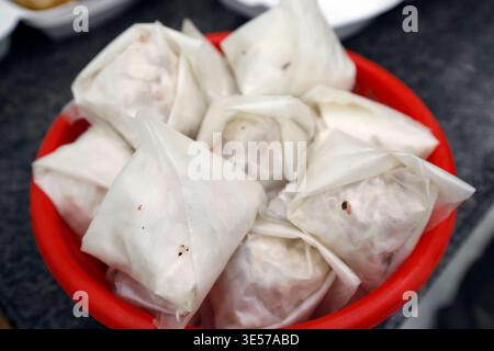 Uncooked fresh spring rolls wrapped in translucent rice paper rest in a red bowl. Haiphong. Vietnam. Stock Photo